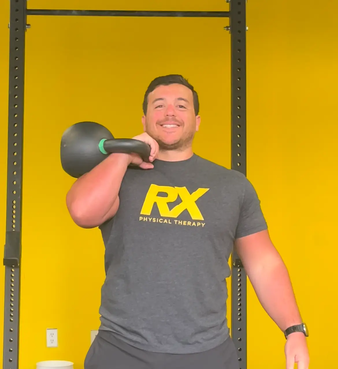 a man holding a kettle while standing in front of a yellow wall.